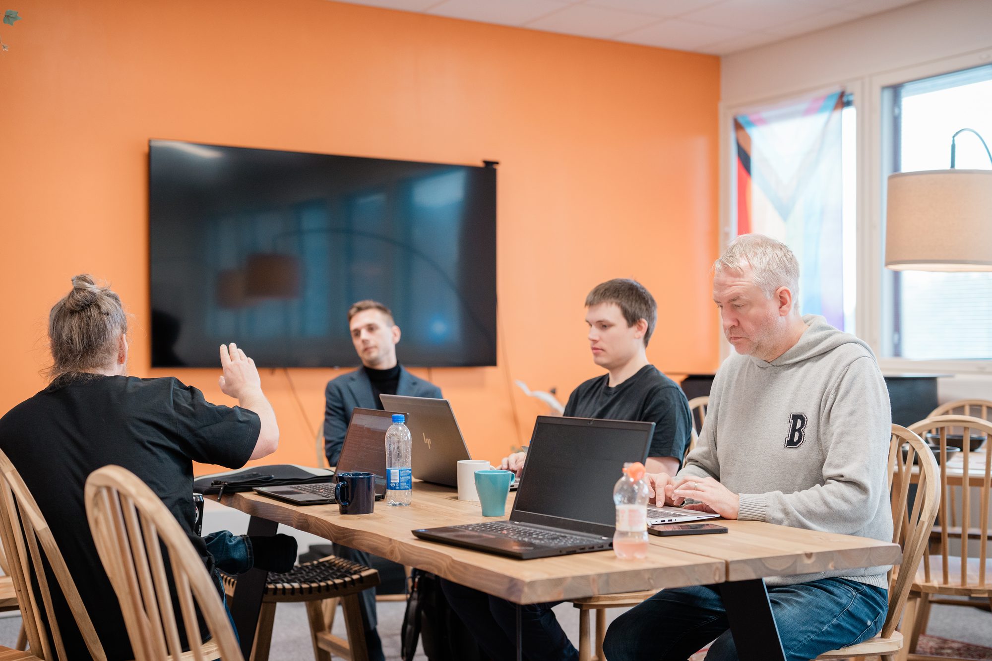 Tiimin palaveri valoisassa huoneessa, jossa on oranssi seinä ja ikkunoita – Yritysjohto – Digitaalinen Polku on sinua varten