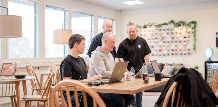 Four people at a wooden table in a spacious office, two of them standing – 10 reasons to take a digital leap
