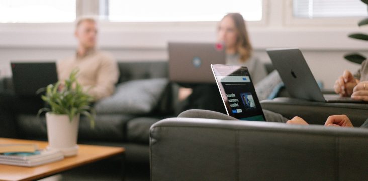 Etualalla läppäri ja nahkanojatuoli, taustalla sumeina kollegat – Siirtyminen Universal Analyticsista Google Analytics 4:ään: uudet ominaisuudet, tietosuojakeskeisyys ja hyödyt liiketoiminnalle