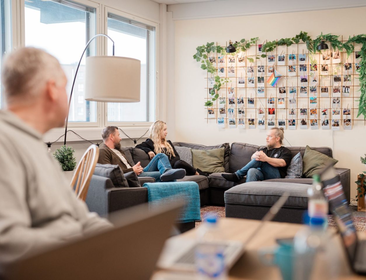 A photo wall and sofas seen past a table with laptops and water bottles – Digital business