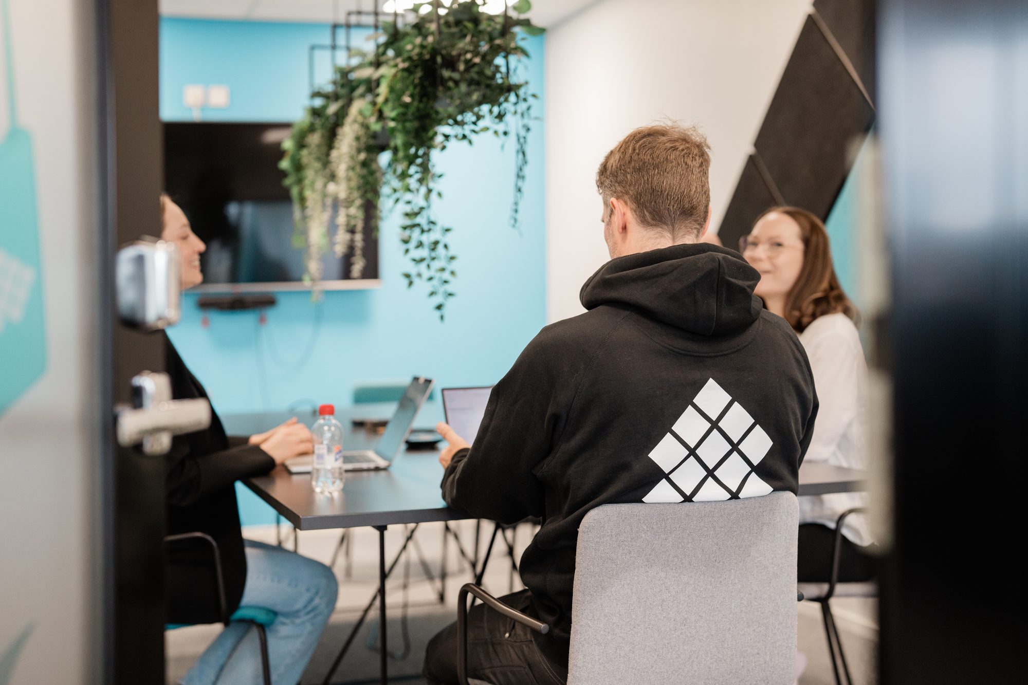 Kolme ihmistä palaveripöydän ääressä huoneessa, jossa on turkoosi seinä ja riippukasveja – Digital Heart Capital kiihdyttää startupeja digisydämellä