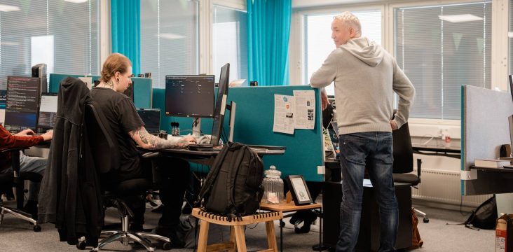 Laaja kuva avokonttorista, etualalla reppu ja puinen jakkara – Responsiiviset komponentit: taulukot