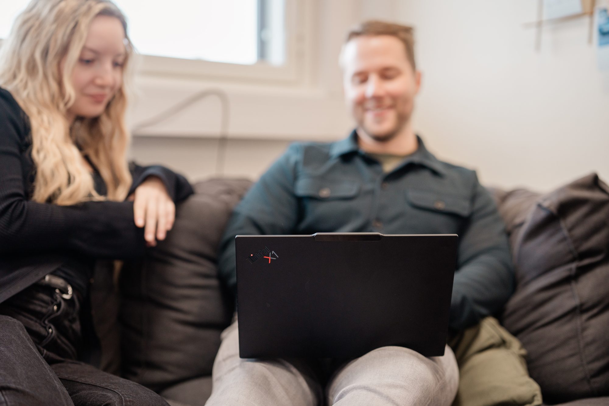 A smiling person with a laptop on their lap on a sofa, a colleague sitting beside them – How to measure and improve customer retention