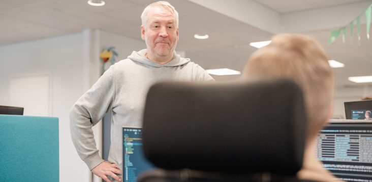 A person in a grey hoodie stands with a hand on their hip, talking to a colleague – Finhai Sealdeal®