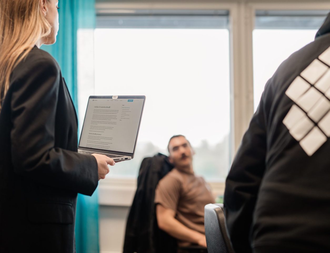 Henkilö seisoo läppäri kädessään ja juttelee istuvan kollegan kanssa – Magento-verkkokauppa