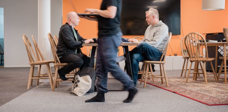Two people work at a wooden table while a colleague walks past – Building a competitive edge through digital ecosystem