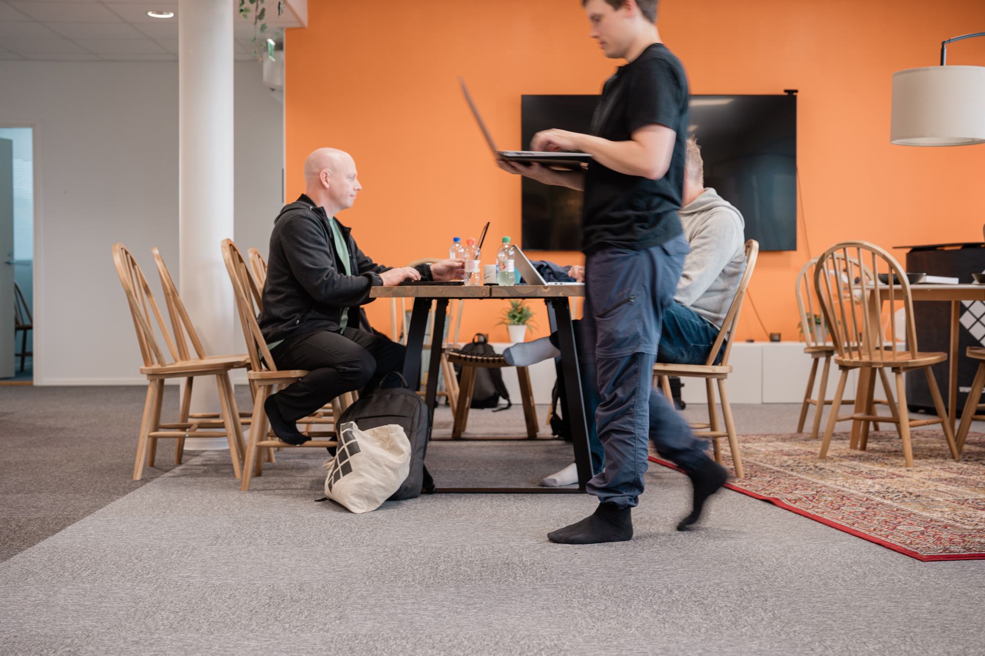 A bald person in a dark jacket works at a wooden table by an orange wall – 7 predictions on the future of Digital Commerce