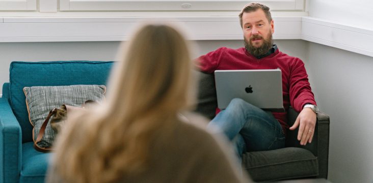 Punaiseen neuleeseen pukeutunut henkilö istuu läppäri sylissään ja kuuntelee – Mikä on IT-auditointi ja milloin se kannattaa tehdä?