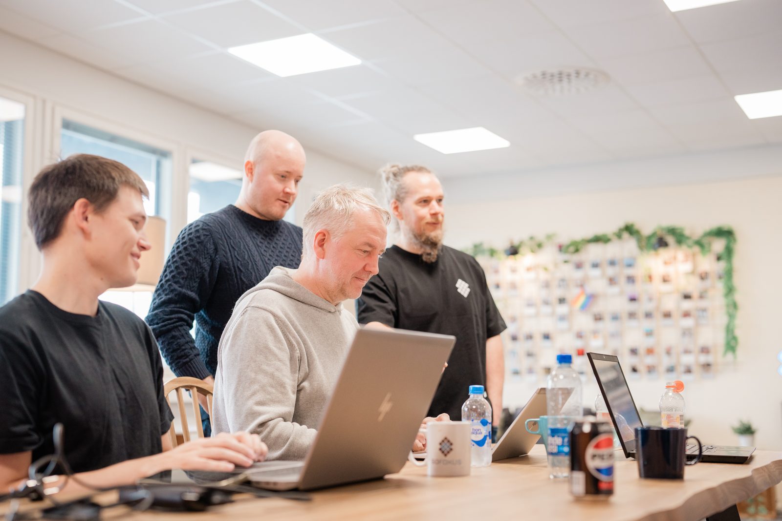 Neljä Sofokuksen asiantuntijaa katsoo yhdessä kannettavan näyttöä valoisassa toimistossa, osa istuu ja osa seisoo / Four Sofokus experts look at a laptop screen together in a bright office, some sitting and some standing