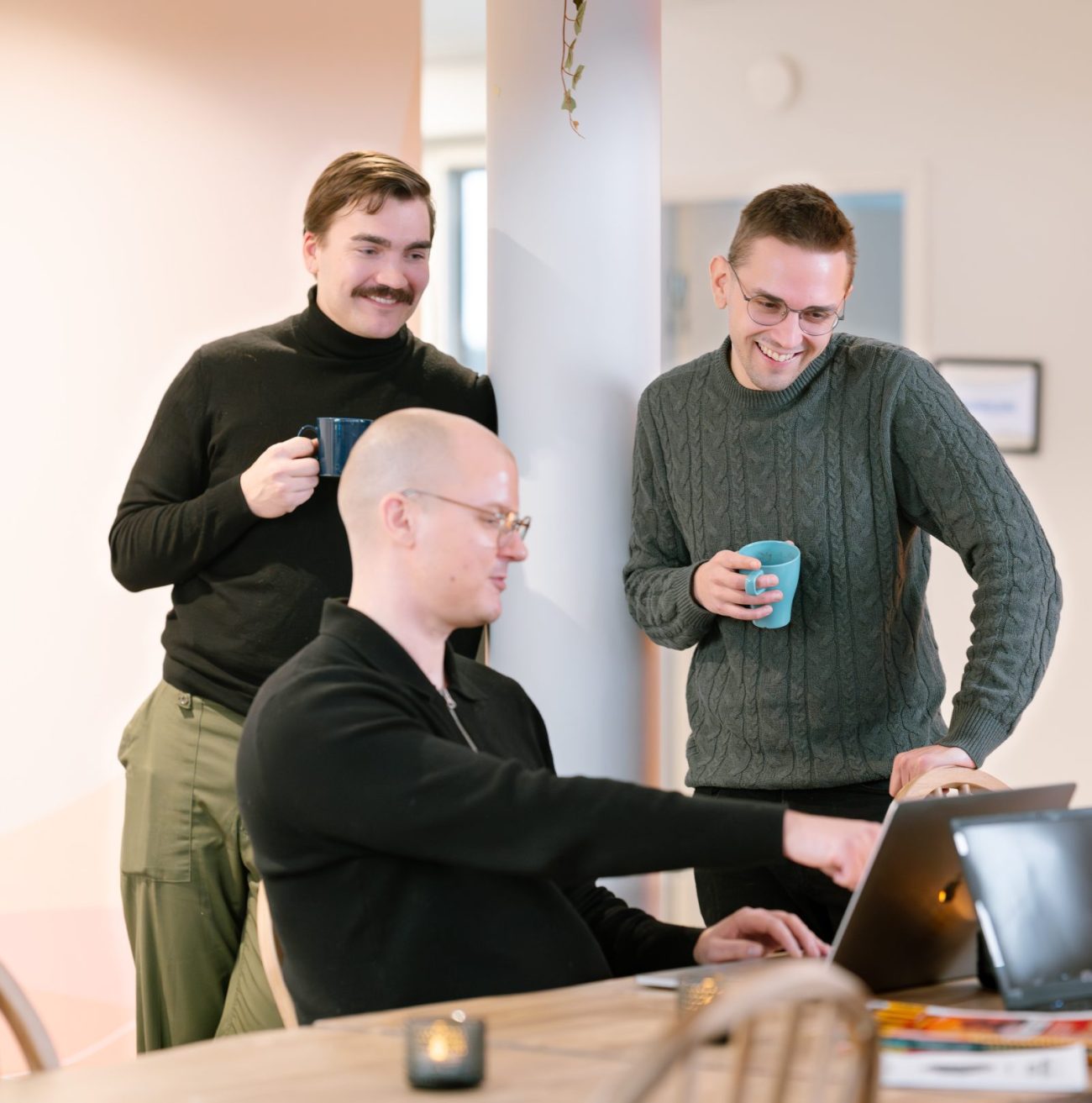 Three Sofokus colleagues chatting over coffee around a laptop at the office