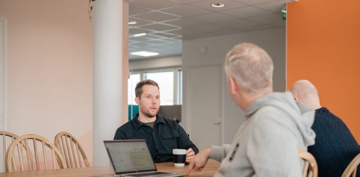 Läppäri ja muki puupöydällä, oikealla oranssi seinä – Mitä tarkoittaa ohjelmiston integraatio ja miksi se voi tuplata kilpailuetusi?