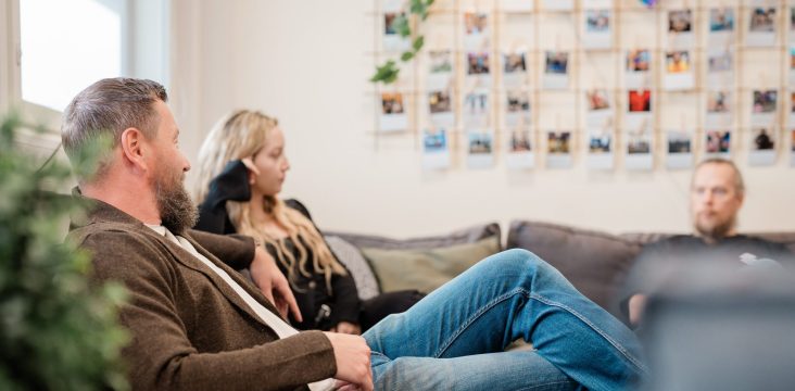 Pikakuvista koottu valokuvaseinä harmaalla sohvalla istuvan kolmikon takana – Säästöä pilvestä tapahtuma Turussa 3.2.2011