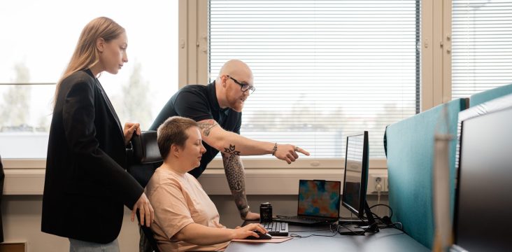 Kolme ihmistä työpisteellä suurten sälekaihdinikkunoiden edessä – WordPress – muutakin kuin blogi?