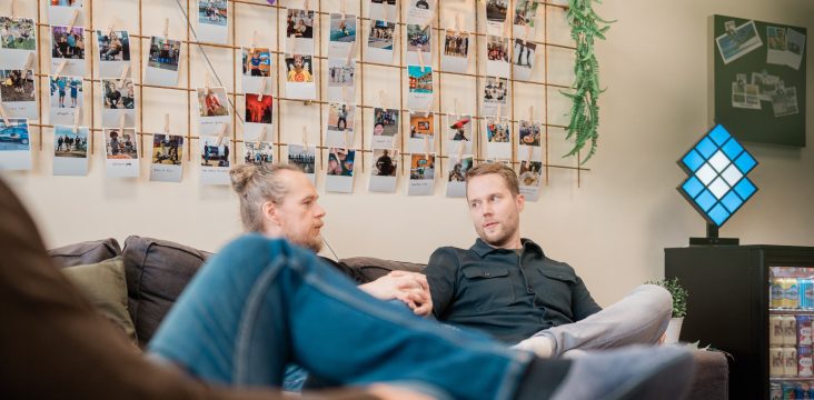Two people laughing on a sofa in front of a photo wall – Venture Design helps you know where to focus