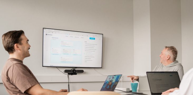 Two people in a meeting room smile while looking at a web page on a wall display – Technology strategy: How to transform from a Tech Slagger to a Tech Forerunner?