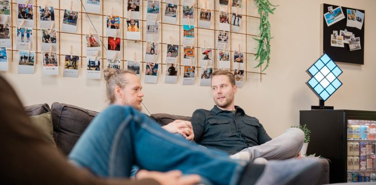Harmaa sohva, valokuvaseinä ja vinoneliön muotoinen valaisin – Venetelakka Ramstedt
